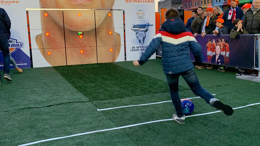 Boy kicking football at precision wall 9-panel with gilette branding with crowd watching