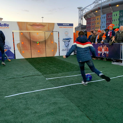 Boy kicking football at precision wall 9-panel with gilette branding with crowd watching