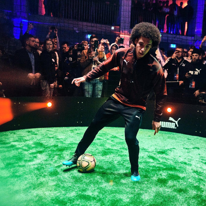 Axel Witsel wearing tracksuit dribbling ball on astro turf inside acura elite icon arena while crowd watch in background