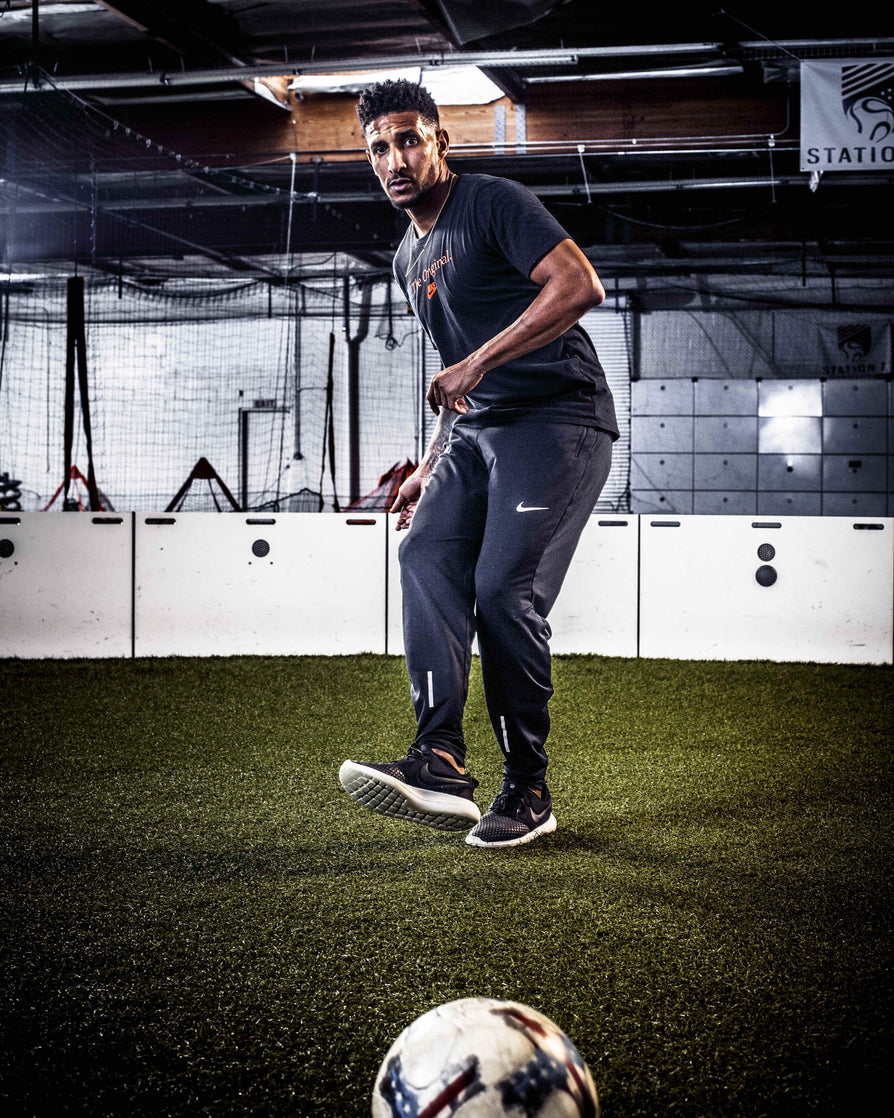 man kicking football towards camera while inside white acura elite esa icon arena