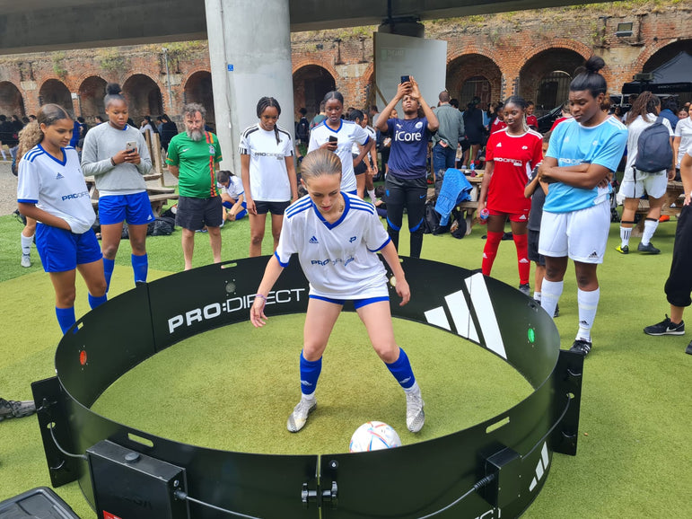Girls wearing football kit playing football using acura elite icon fast feet with spectators