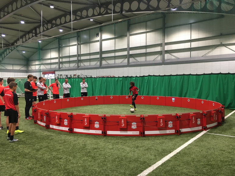 Children playing soccer on a red liverpool branded acura icon arena 8m in an indoor sports facility.