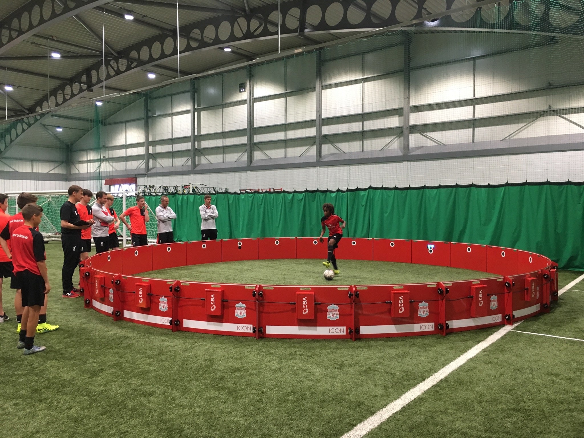 Children playing soccer on a red liverpool branded acura icon arena 8m in an indoor sports facility.