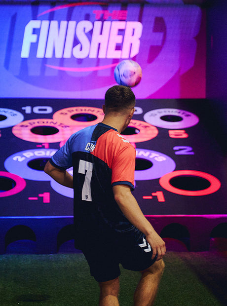man playing football with acura elite esa panenka inside facility with pink background and colourful targets