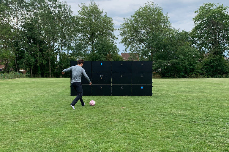 man kicking football at acura elite precision wall 12 panel outside on field