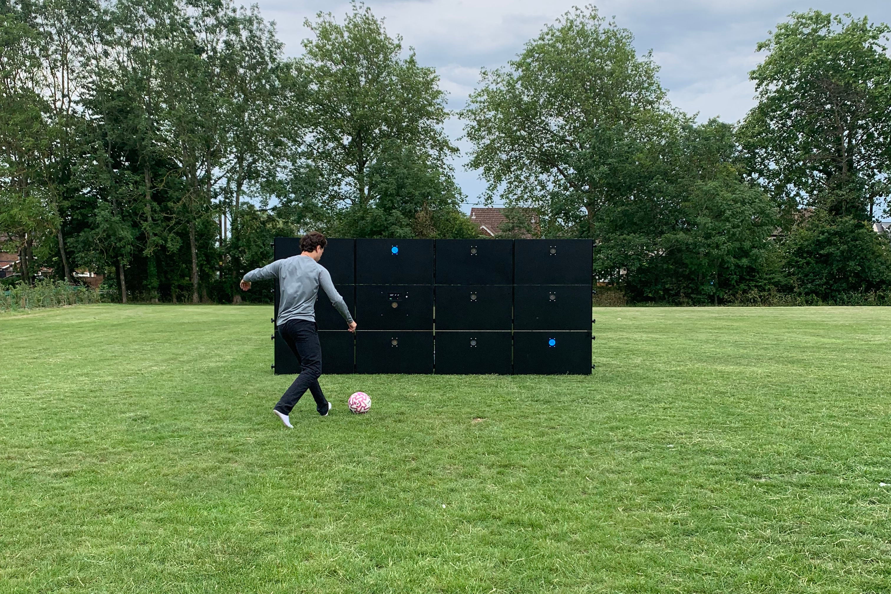 man kicking football at acura elite precision wall 12 panel outside on field