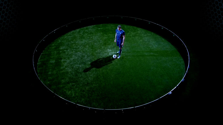 A thumbnail of a soccer/football player in a blue uniform stands on a green field inside a ICON Arena, casting a long shadow against a dark background.