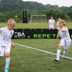 Children playing soccer on a field inside acura arena 8m 16-panel
