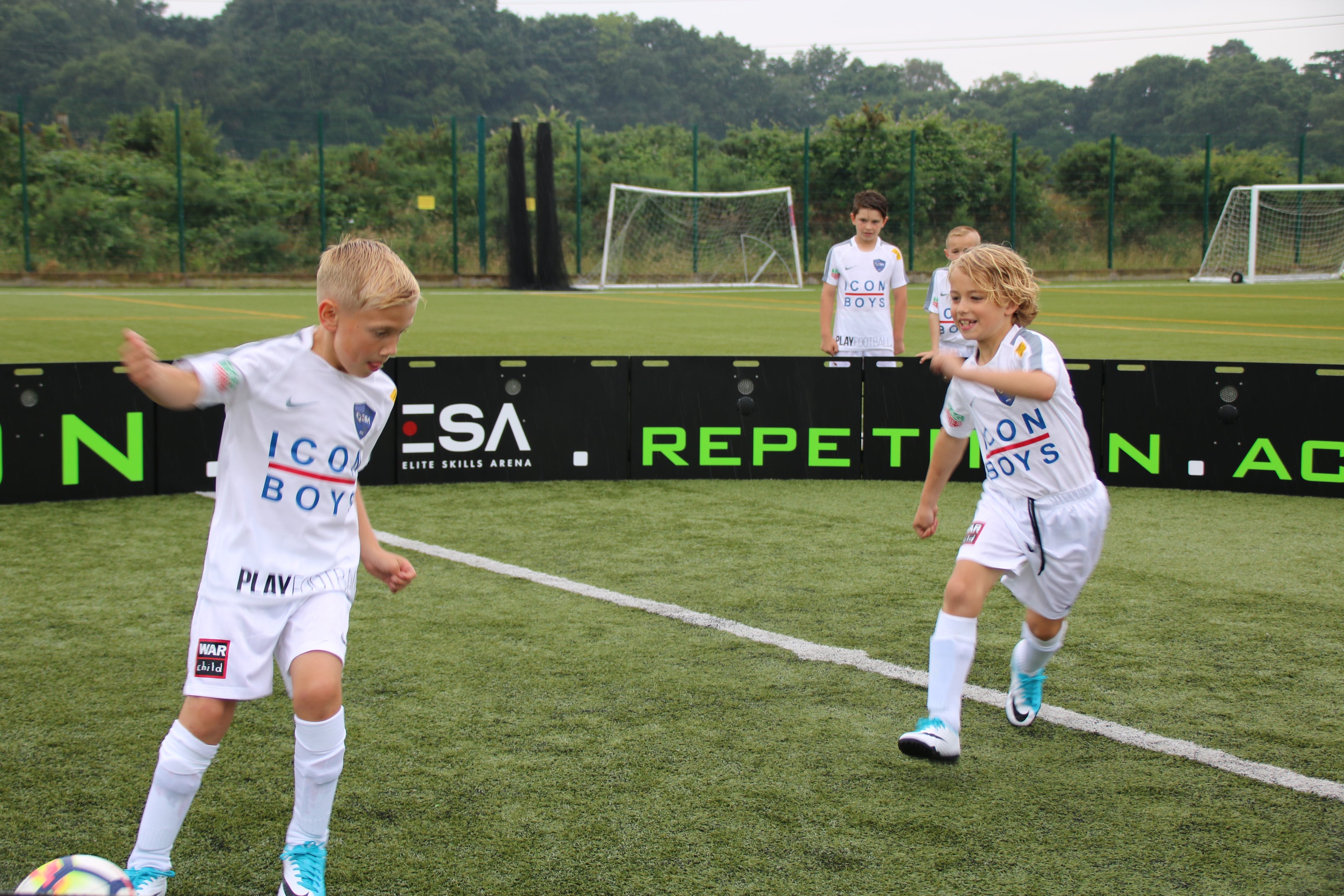 Children playing soccer on a field inside acura arena 8m 16-panel