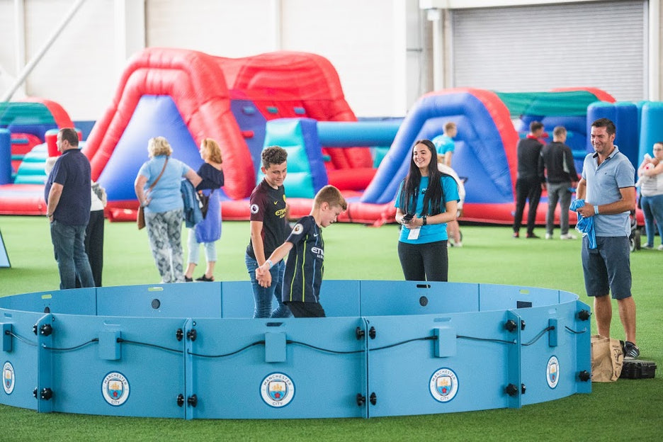 family watching boy play football in icon arena 4m 12-panel with manchester city branding and inflatables in the background