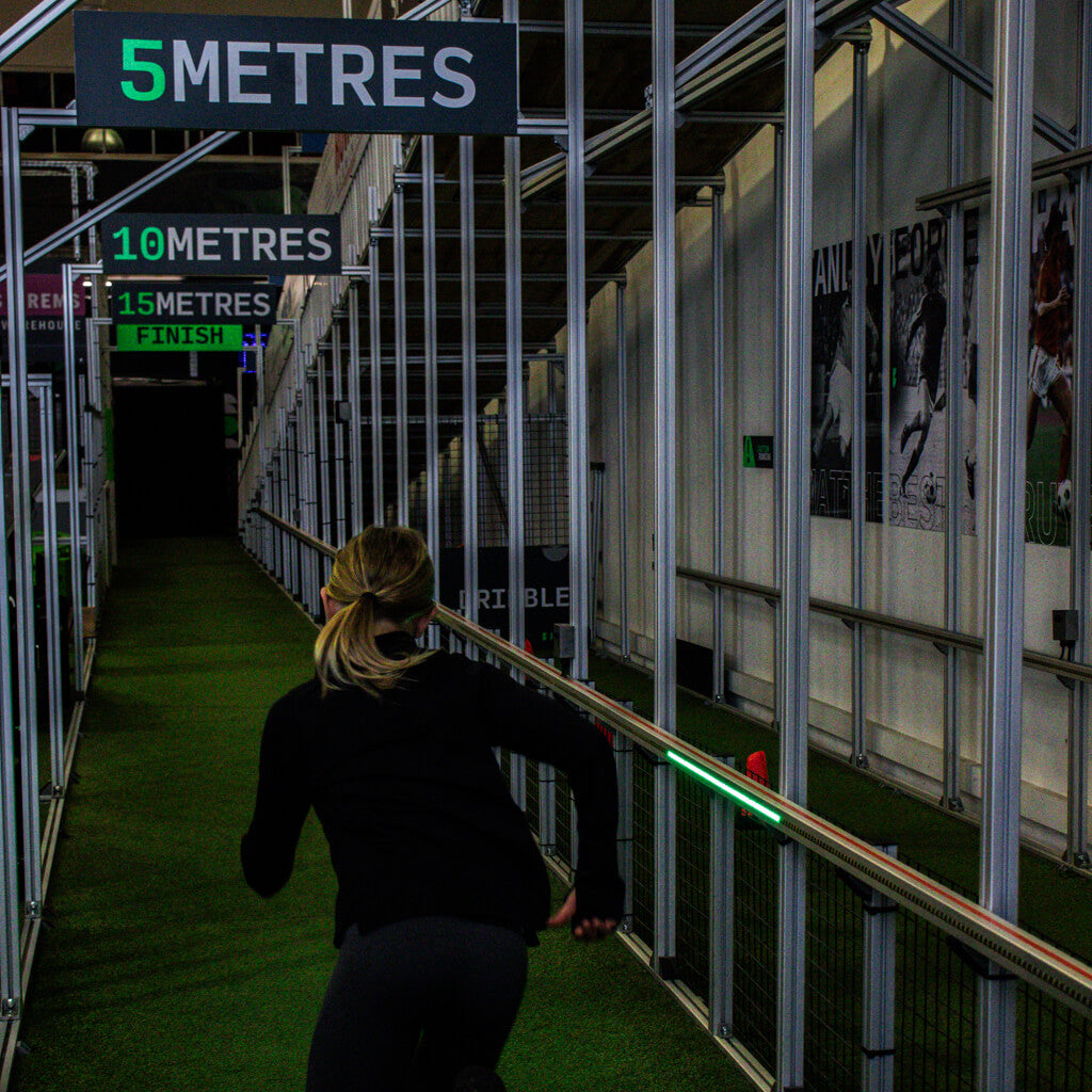 girl in a black training outfit running down sprint lane with 5 metre signs above