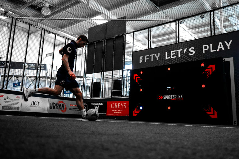 man kicking football at acura 9-panel precision wall at indoor training center