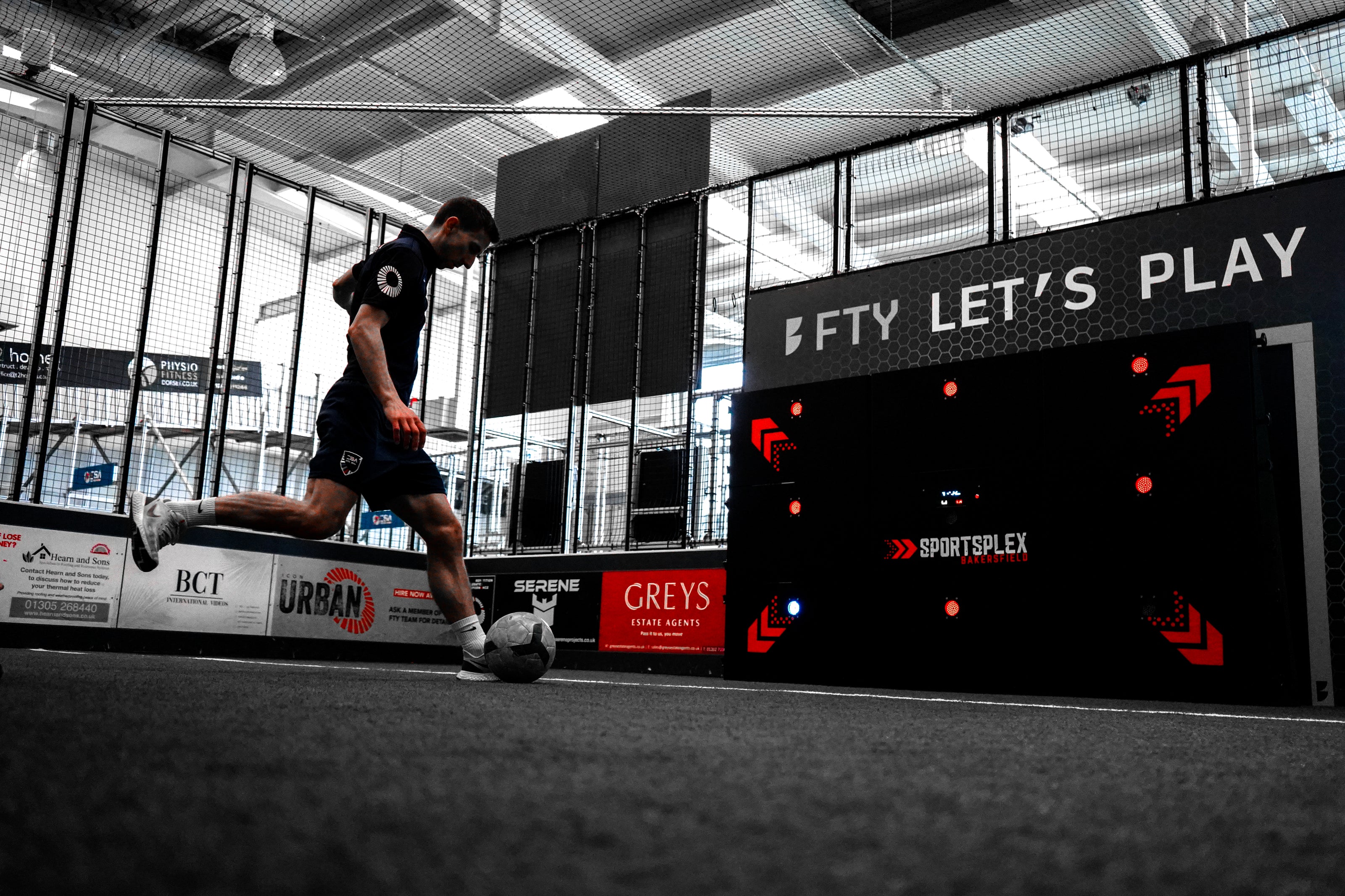 man kicking football at acura 9-panel precision wall at indoor training center