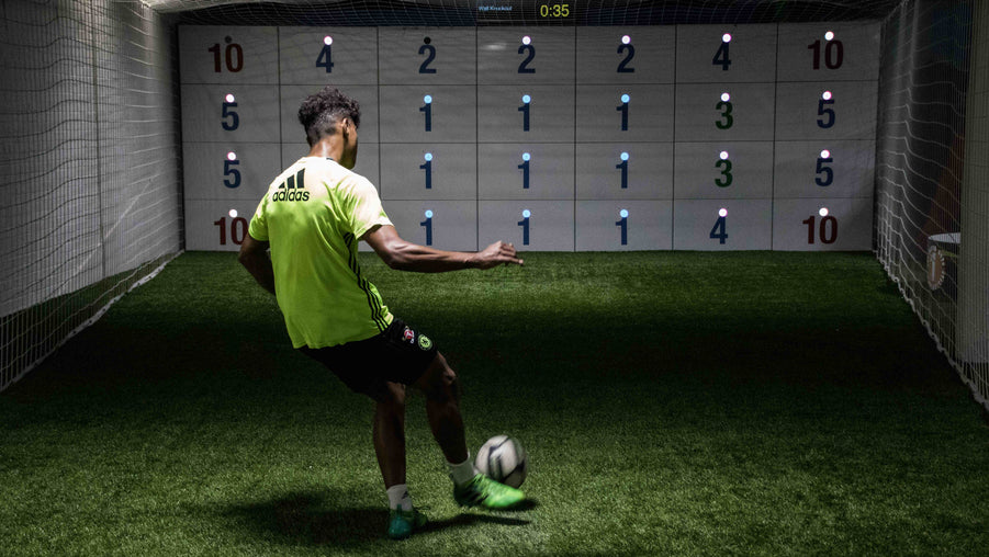 man in yellow football kit kicking ball at precision wall 28 panel with numbered panels and blue LED lights