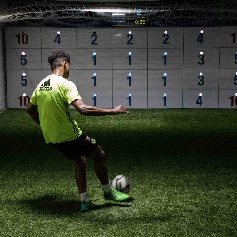 man in yellow football kit kicking ball at precision wall 28 panel with numbered panels and blue LED lights