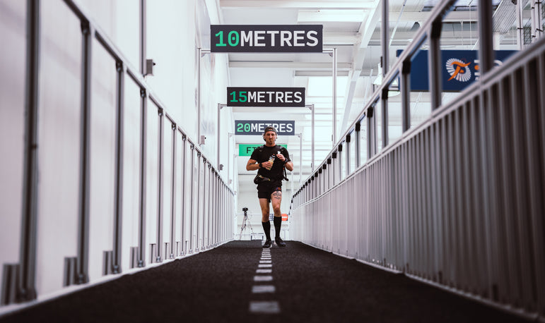 man in training gear with water bottle walking down training lane (sprint) inside training facility