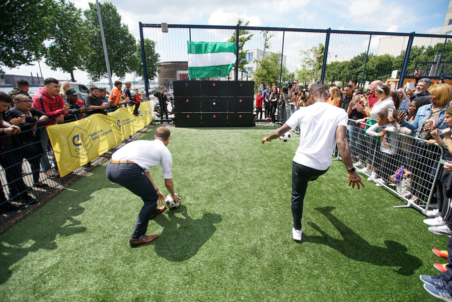 two men kicking footballs at acura elite precision wall 9 panel with spectators at sides