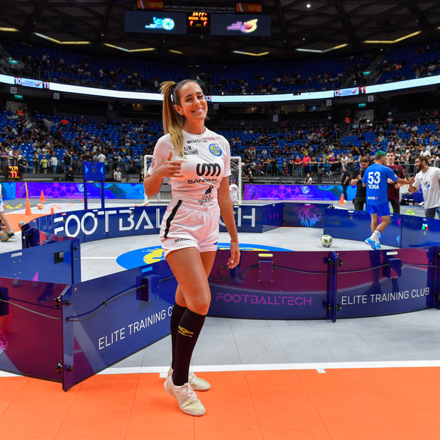 woman posing beside acura elite icon v2 equipment in a sports arena